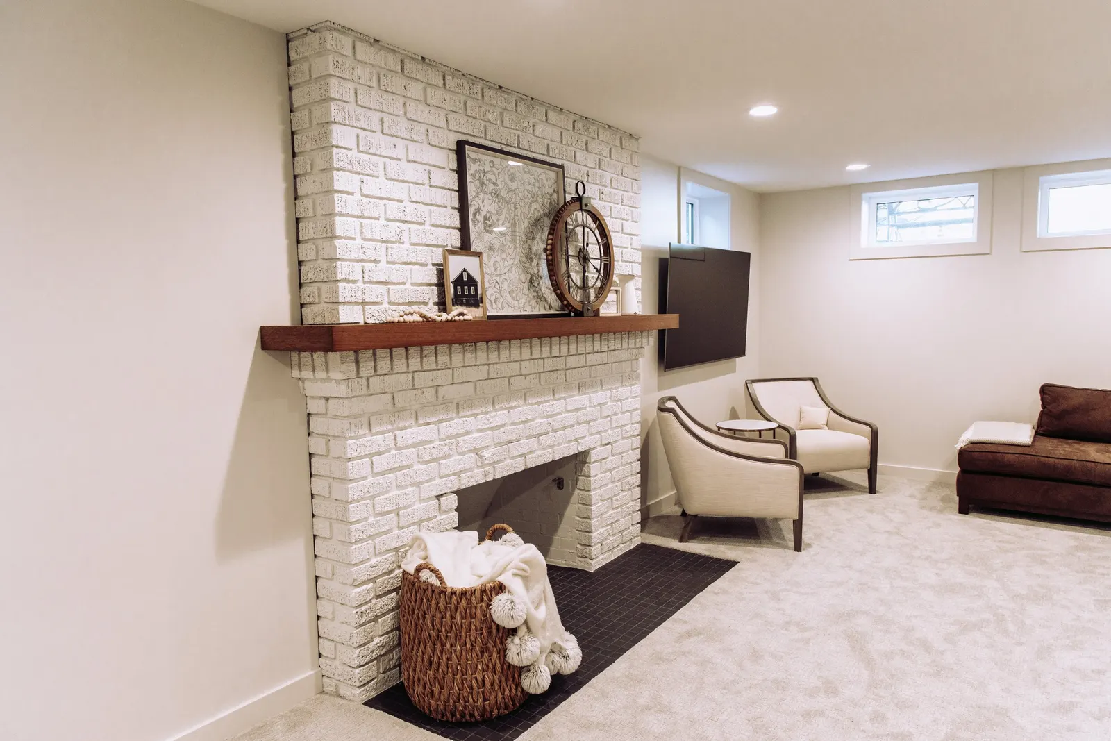 1922 Basement Remodel, carpet, brick fireplace, custom wood mantel, white cabinets, matte black hardware, matte black sconces, open shelves, floating wood shelves, custom woodworking, Lincoln Nebraska, professional contractors, craftsmanship.