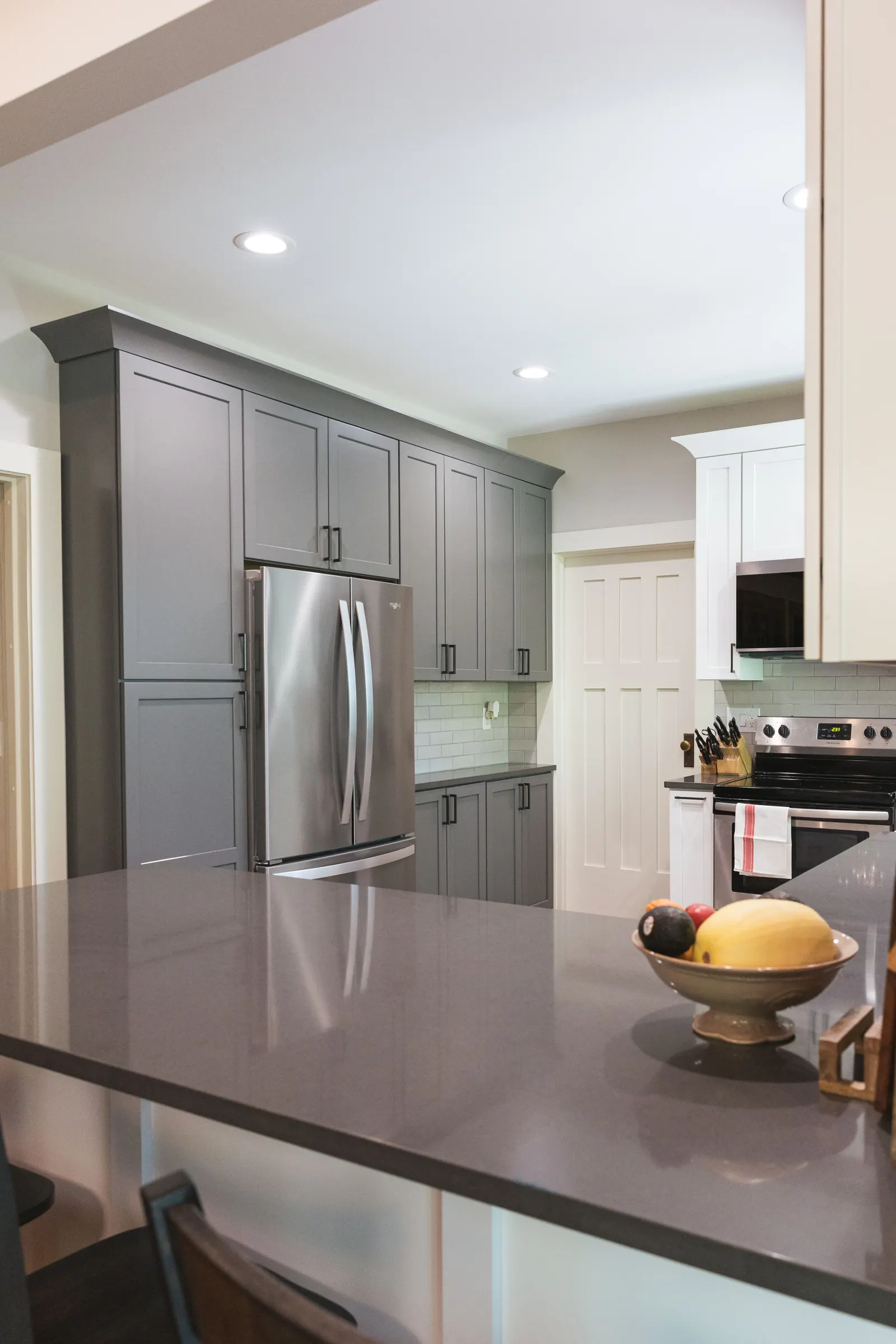 Gray pantry cabinets and the refrigerator seen across the quartz peninsula.
