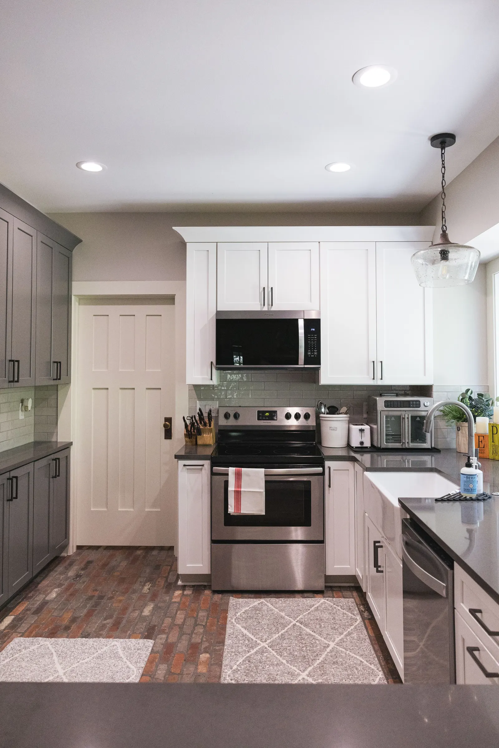 The range wall with white upper cabinets, gray tall cabinets, and a view toward the bay window.