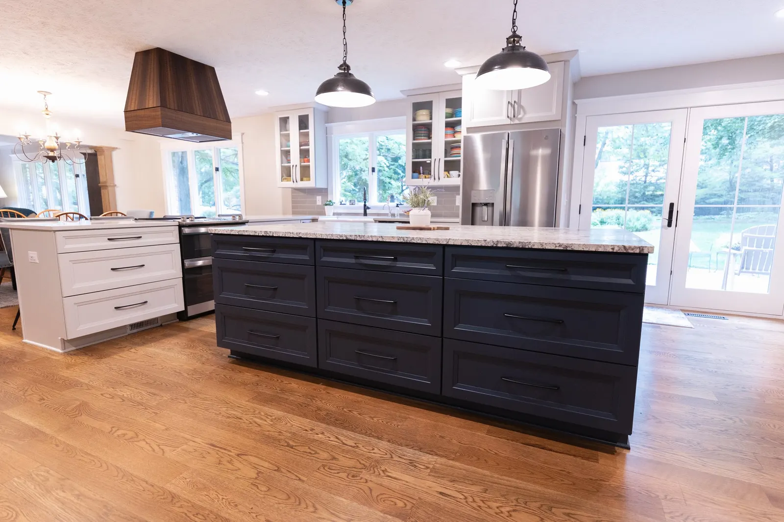 Modern kitchen with black and white cabinets, granite countertops, stainless steel refrigerator, wooden floor, and sliding glass doors to outdoors.