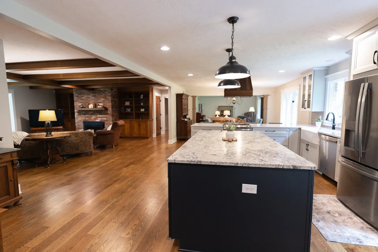 1974 Whole Home Remodel, open-concept kitchen and living room with hardwood flooring, white cabinetry, quartz countertops, and a large kitchen island with pendant lights, custom wood beams, dual tone kitchen, matte black hardware.