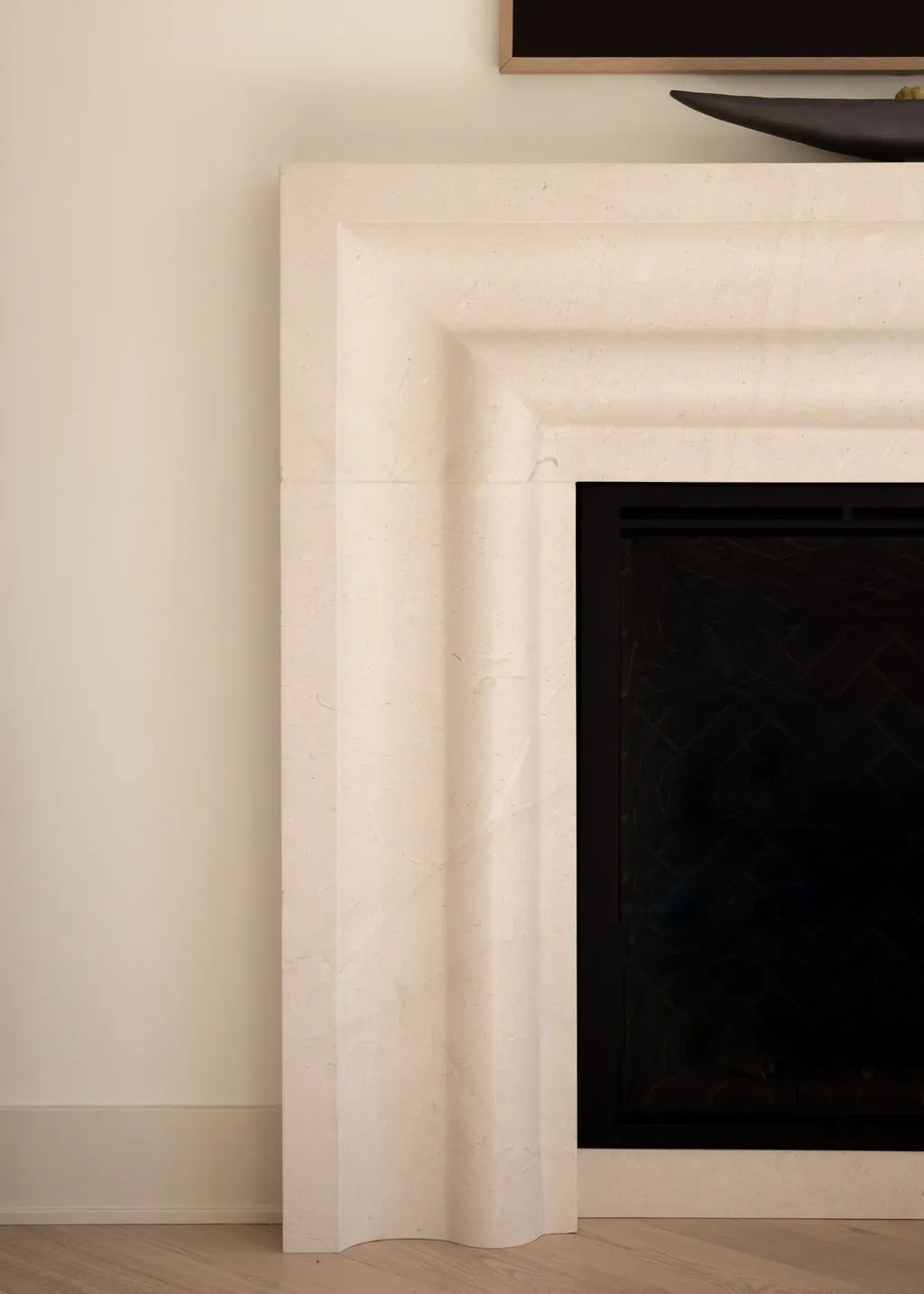 Close-up of a fireplace with a beige marble mantel in a room with light-colored walls and wooden flooring.