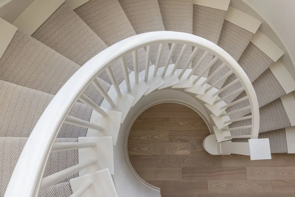 Overhead view of a curved staircase with beige carpeting and a wooden floor at the bottom.