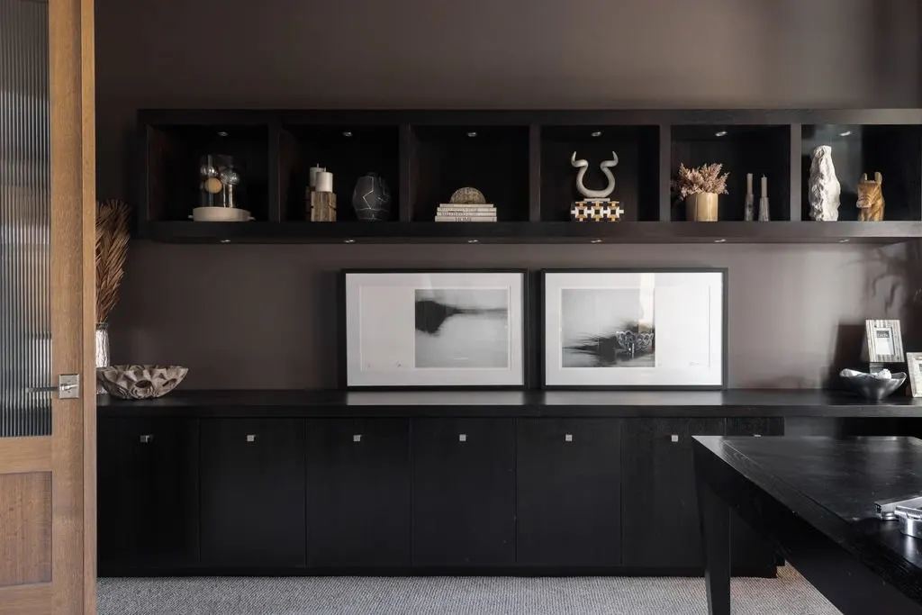 Dark wood sideboard with two black and white abstract art prints on top, decorated with framed photos and bowls, and open shelves above holding vases, sculptures, and decorative objects in a modern interior.