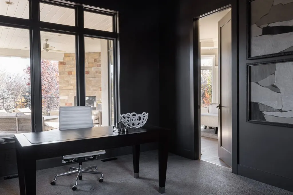 A modern home office with a black desk, white swivel chair, and large window showing an outdoor patio.