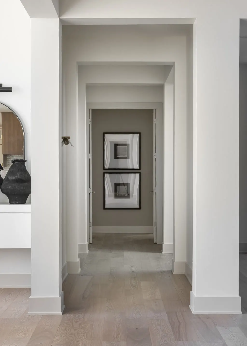 A hallway with white walls leading to a small space with two framed pictures hanging on a gray wall.