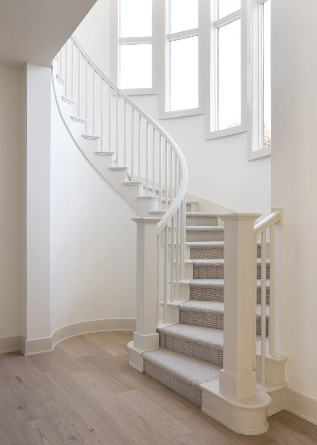 Interior view of a staircase with white railings, carpeted steps, and large windows allowing natural light to fill the space.