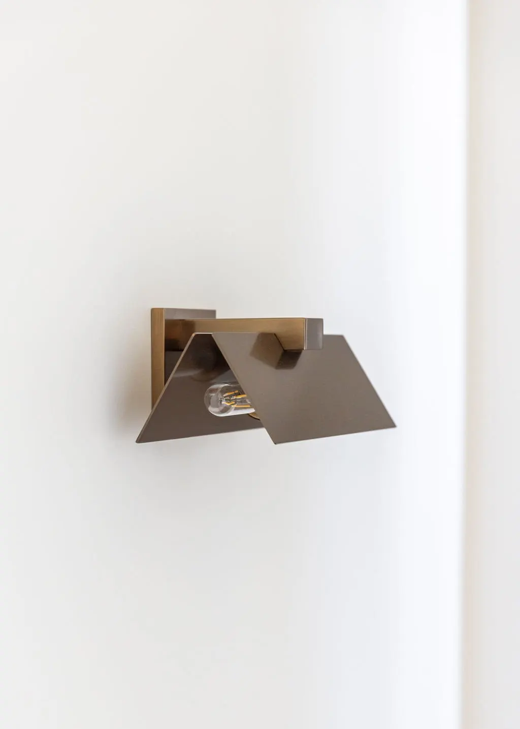 Modern wall-mounted light fixture with metal shade and exposed light bulb on a white wall.