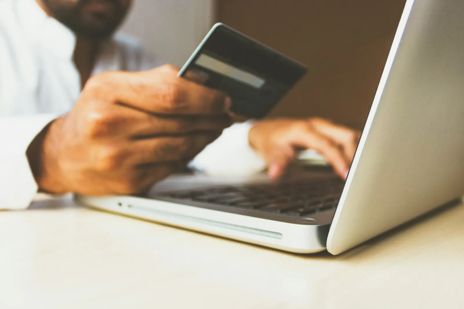 Person holding a credit card and using a laptop at a desk.