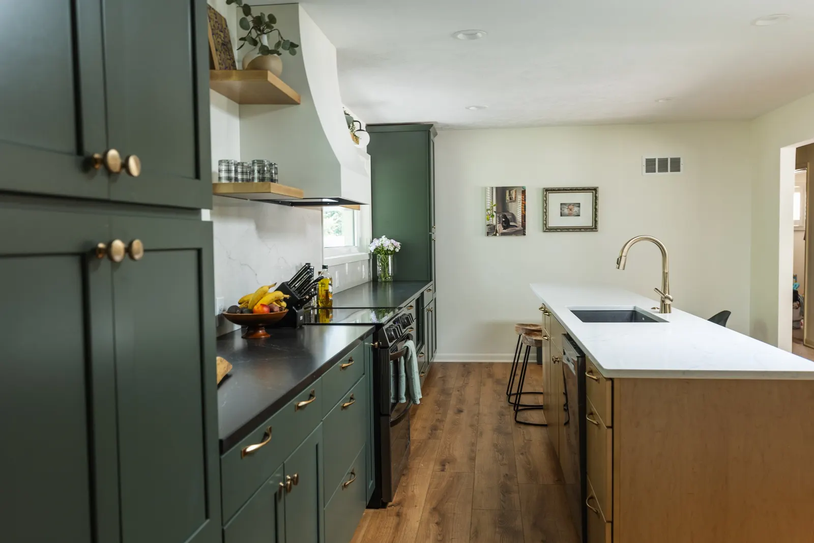 Modern kitchen with green cabinets, a white marble island, and wooden flooring.